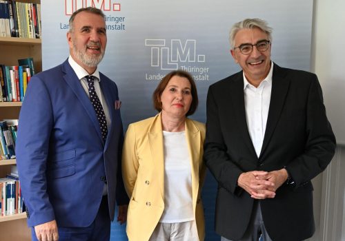 Zwei Männer und eine Frau stehen vor einem TLM.-Banner