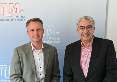 Zwei Männer vor dem TLM-Banner schauen in die Kamera