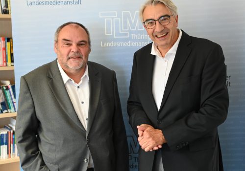Zwei Herren in dunklen Anzügen stehen nebeneinander.