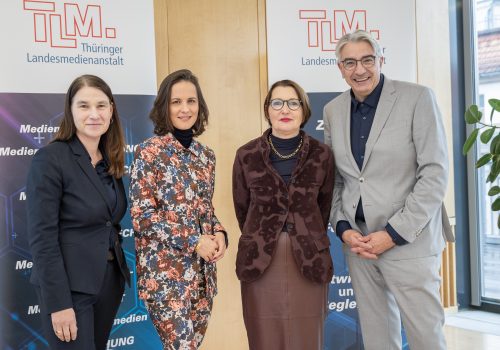 Drei Frauen und ein Mann stehen vor TLM-Bannern