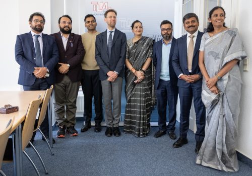 Sechs Männer und zwei Frauen stehen vor einem Banner der TLM