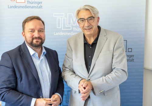 Zwei Männer stehen nebeneinander und lächeln.