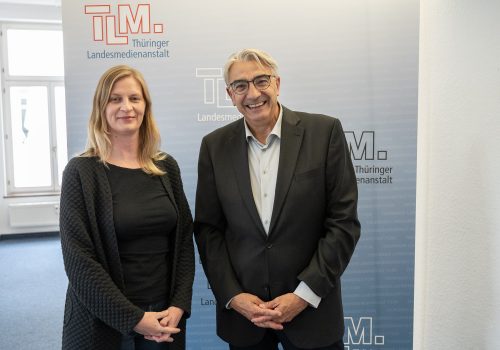 Eine Frau und ein Mann stehen vor einem TLM-Banner