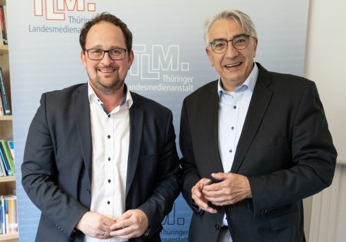 Zwei Männer stehen nebeneinander und lächeln in die Kamera