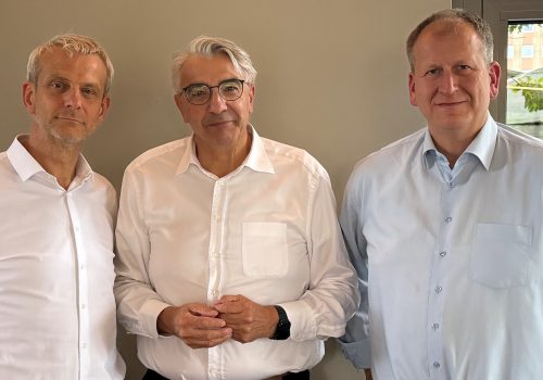 drei Männer in hellen Hemden stehen nebeneinander