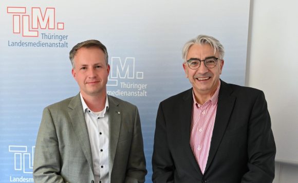 Zwei Männer vor dem TLM-Banner schauen in die Kamera