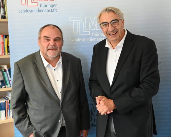 Zwei Herren in dunklen Anzügen stehen nebeneinander.