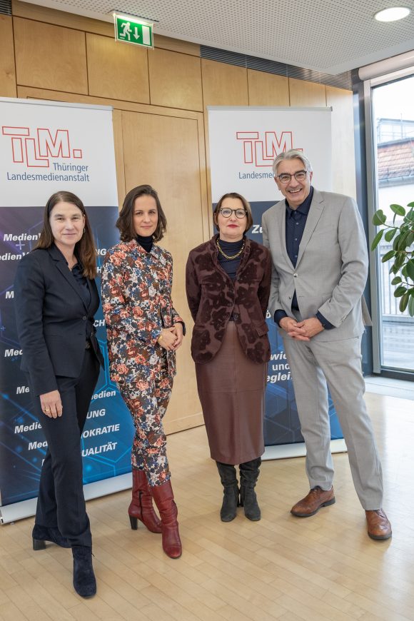 Drei Frauen und ein Mann stehen vor TLM-Bannern