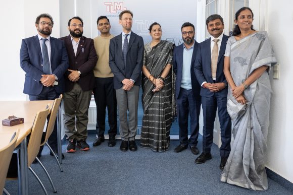 Sechs Männer und zwei Frauen stehen vor einem Banner der TLM