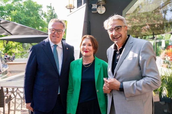 Eine Frau rechts und links ein Mann stehen nebeneinander und lächeln in die Kamera