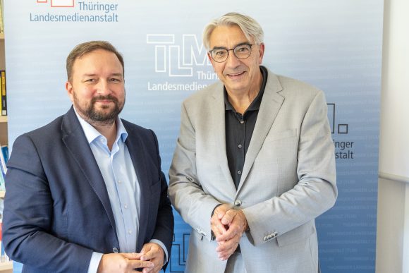 Zwei Männer stehen nebeneinander und lächeln.