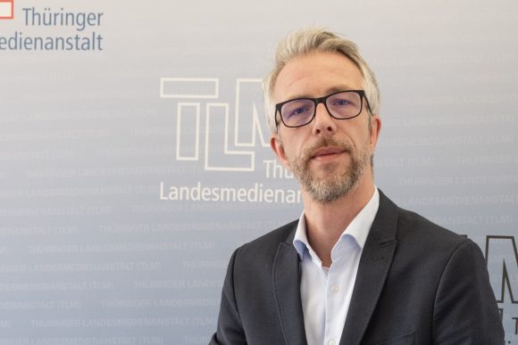 Ein Mann mit schwarzer Brille und Bart schaut in die Kamera.