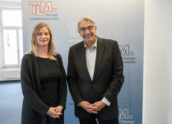 Eine Frau und ein Mann stehen vor einem TLM-Banner