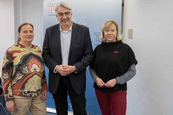 Zwei Frauen und ein Mann stehen nebeneinander und lächeln in die Kamera