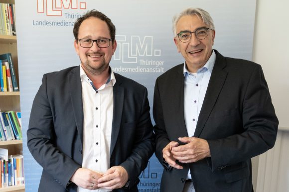 Zwei Männer stehen nebeneinander und lächeln in die Kamera