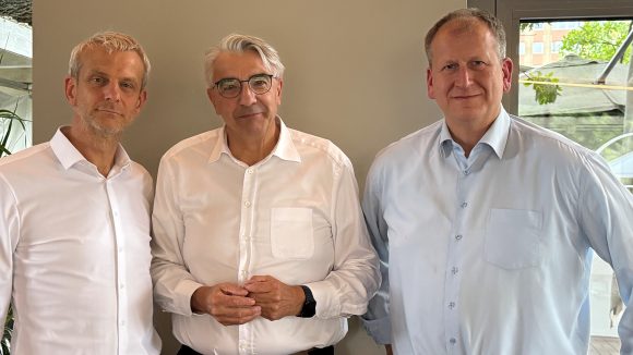 drei Männer in hellen Hemden stehen nebeneinander