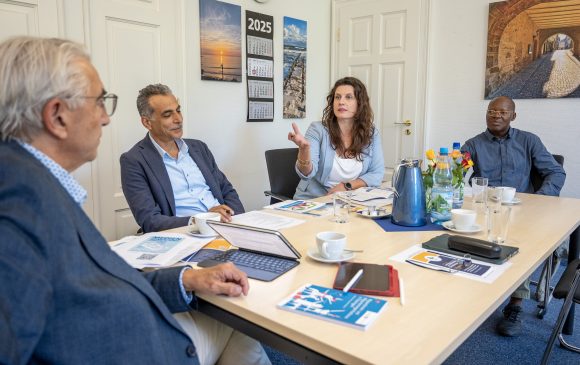 Drei Männer und eine Frau sitzen an einem Tisch und reden miteinander.