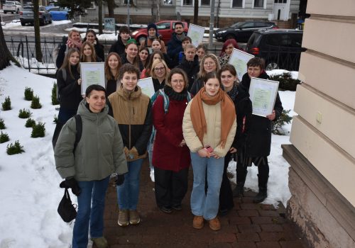 Viele jungen Menschen stehen zusammen in Winterjacken im Freien und halten ihre Medienscout-Urkunden hoch
