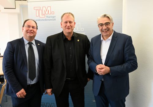 Drei Männer stehen nebeneinander und lächeln in die Kamera