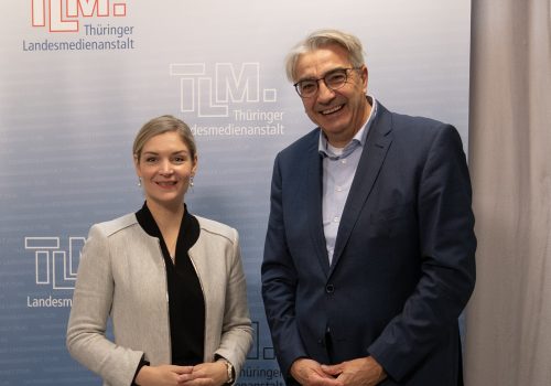 Eine Frau und ein Mann stehen nebeneinander und lächeln in die Kamera.