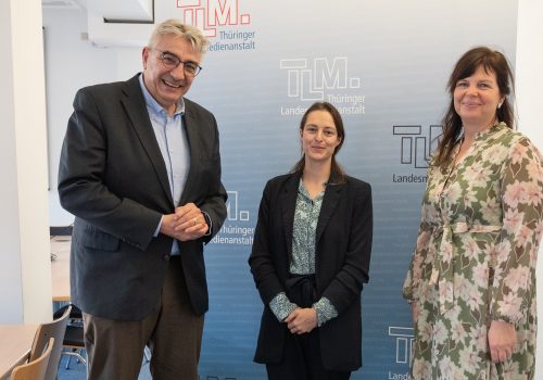 Ein Mann und zwei Frauen stehen nebeneinander und lächeln in die Kamera.