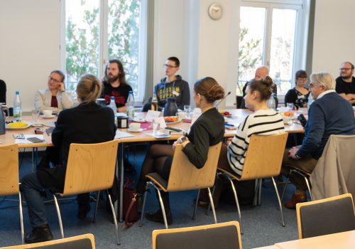 Viele Menschen sitzen an einem großen Tisch und unterhalten sich.