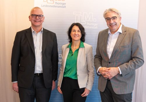 Eine Frau und zwei Männer stehen nebeneinander und lächeln in die Kamera.