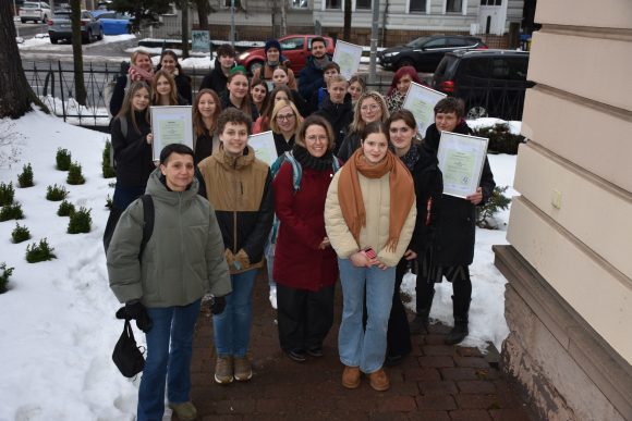 Viele jungen Menschen stehen zusammen in Winterjacken im Freien und halten ihre Medienscout-Urkunden hoch