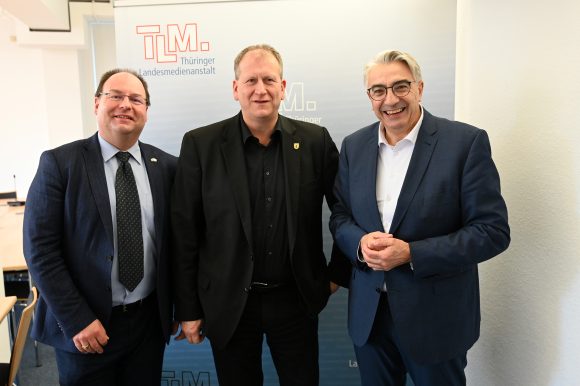 Drei Männer stehen nebeneinander und lächeln in die Kamera