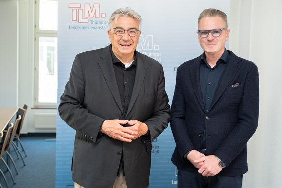 Zwei Männer in dunklen Anzügen stehen nebeneinander und schauen Richtung Kamera.