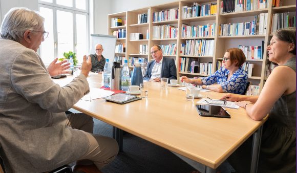 Drei Männer und zwei Frauen sitzen an einem Besprechungstisch und reden