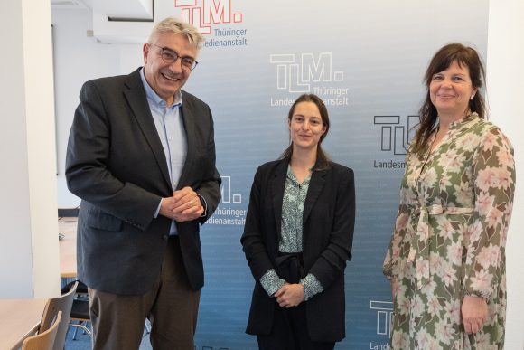 Ein Mann und zwei Frauen stehen nebeneinander und lächeln in die Kamera.