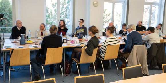 Viele Menschen sitzen an einem großen Tisch und unterhalten sich.
