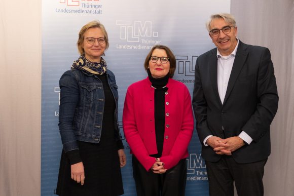 Zwei Frauen und ein Mann stehen nebeneinander und lächeln in die Kamera.