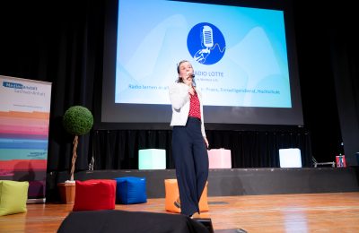 Eine Frau spricht auf der Bühne ins Mikrofon