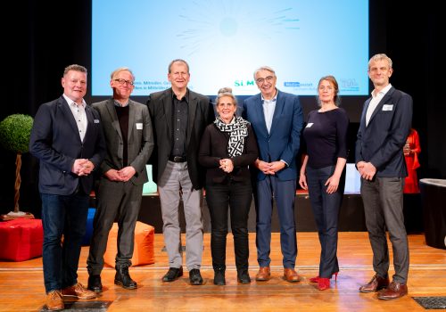 2 Frauen und 5 Männer stehen auf der Bühnen zum Gruppenbild