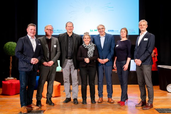 2 Frauen und 5 Männer stehen auf der Bühnen zum Gruppenbild