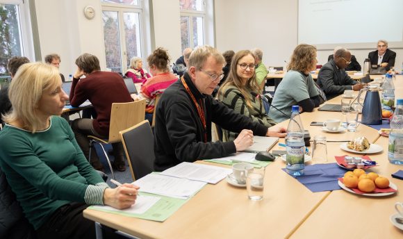 Viele Menschen sitzen in einem Raum an Tischen und beraten sich.